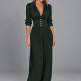 Dua York model wearing the dark-green Elvira pleated maxi dress with four gold buttons against a grey studio background