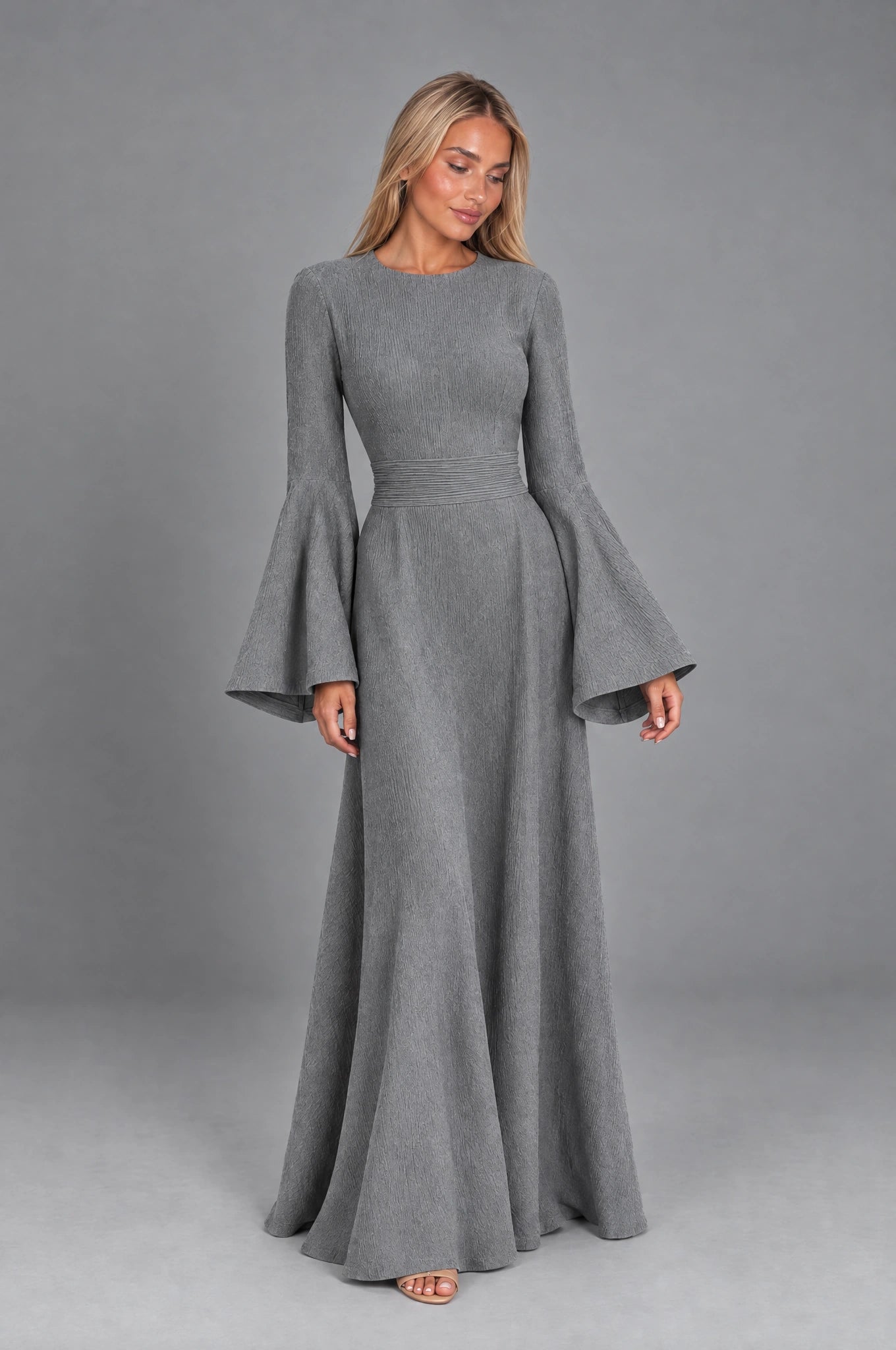 Dua York model wearing the grey Selene floor-length dress with bell sleeves against a grey studio background